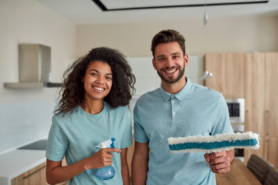 Portrait of happy male and female professional cleaners in uniform holding cleaning supplies